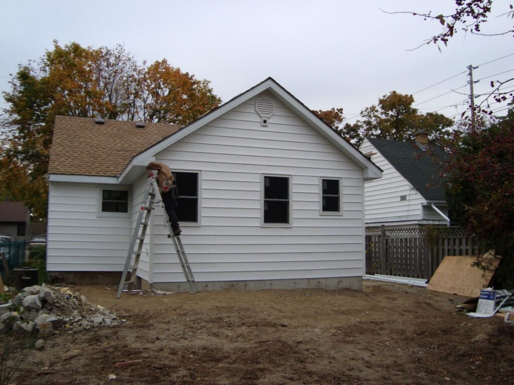 Worker on ladder renovating exterior of house during home improvement project