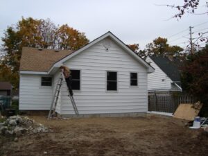 Worker on ladder renovating exterior of house during home improvement project